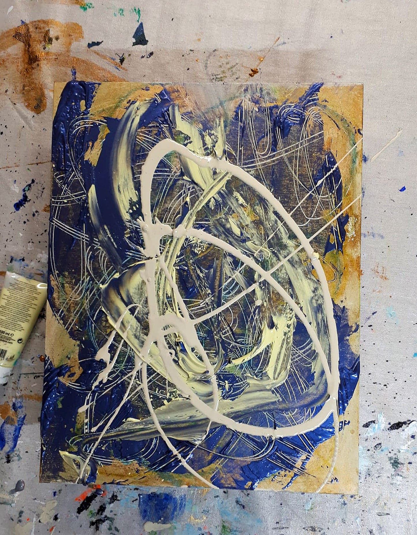 Oblivion' (2018) by Audrey Néron – Freshly painted abstract artwork in the artist's studio, featuring dynamic swirls of deep blue, cream, and gold tones with bold acrylic and pastel textures on a canvas panel. The work sits on a paint-splattered surface, showcasing the creative process.