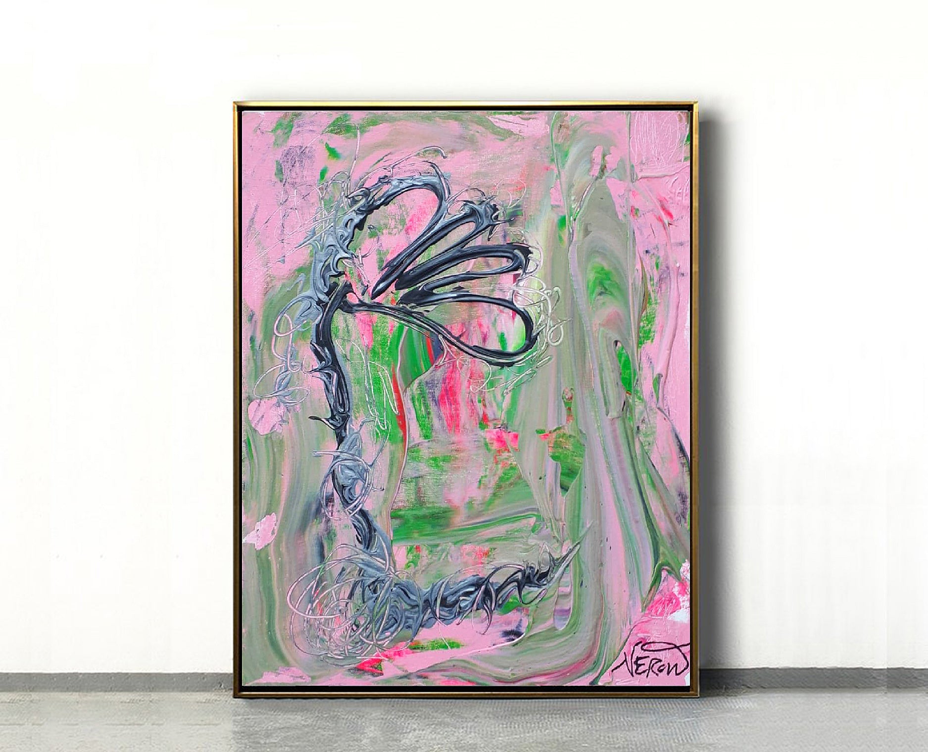 Framed view of the abstract painting Louna (2019) by Audrey Néron, featuring a stylized floral black and grey form over a fluid pink and green background. The artwork is displayed against a white wall on a grey floor, set in a thin gold frame.