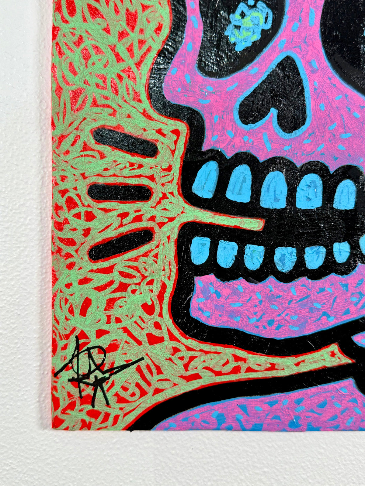 Detail showing the artist’s signature on a Pop Icon skull painting by Audrey Néron, with bold black outlines, pink skull, and green-red textured acrylic background.